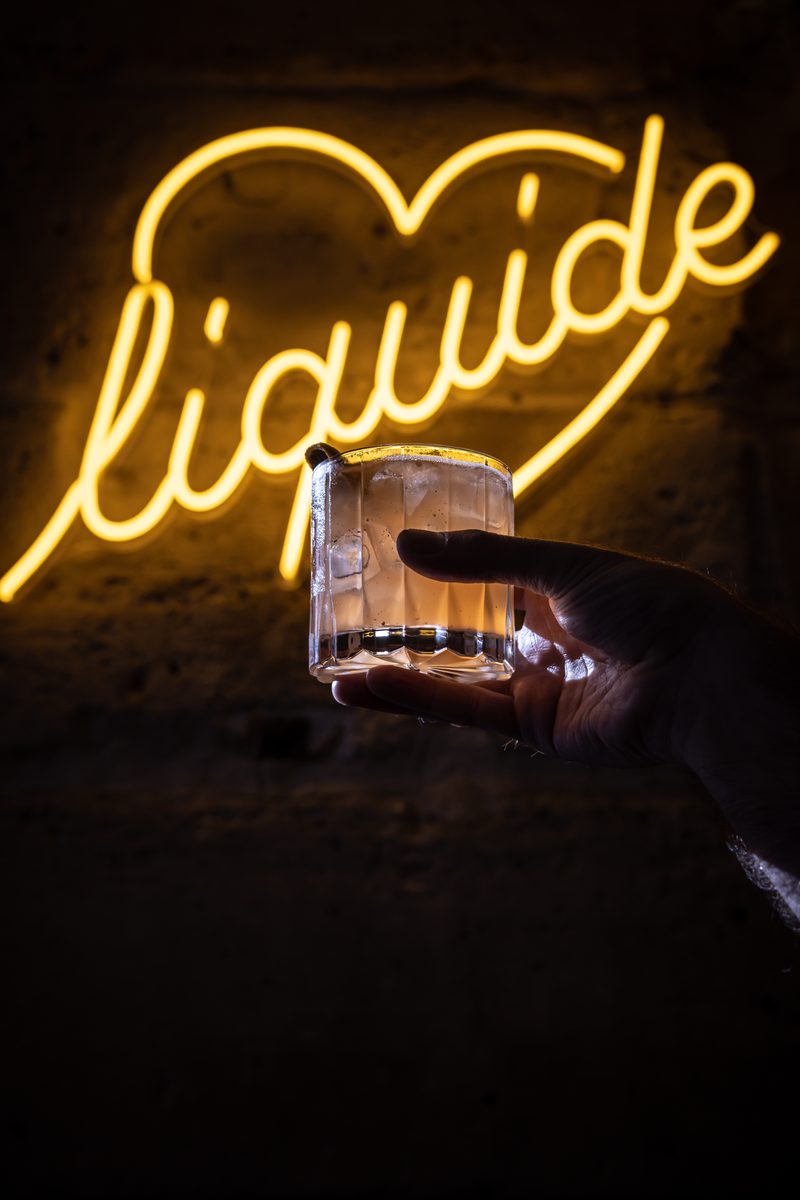 Un cocktail devant l’enseigne néon Liquide